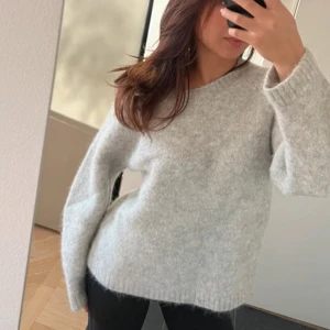 Grå alpacka tröja - Mysig grå tröja i en mjuk alpackablandning. Perfekt för kyliga dagar med sin avslappnade passform och långa ärmar. Tröjan har en enkel design som gör den lätt att matcha med olika outfits.