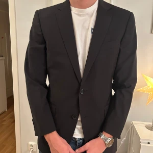 Svart kavaj från Massimo Dutti - Elegant svart kavaj från Massimo Dutti med två knappar framtill. Perfekt för en stilren look. Passar utmärkt till både formella och semi-formella tillfällen.