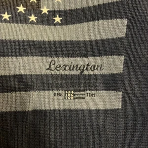 Blå tröja från Lexington - Säljer en blå tröja från Lexington med ett amerikanskt flaggmönster och stjärnor på framsidan. Tröjan är tillverkad i 100% bomull och har långa ärmar med ribbade muddar. Perfekt för en avslappnad stil.