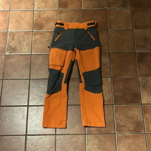 Orange och svarta byxor från Neomondo - Säljer ett par coola orange och svarta byxor från Neomondo. Byxorna har flera praktiska fickor och justerbar midja.