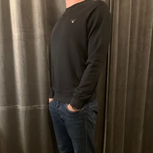 Svart sweatshirt från Gant - Säljer en stilren svart sweatshirt från Gant med rund hals och diskret logga på bröstet. Perfekt för en avslappnad look.
