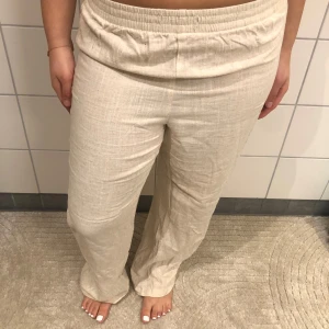 Beige linnebyxor - Snygga och bekväma beige linnebyxor med en avslappnad passform. Perfekta för varma dagar med sin lätta och luftiga känsla. De har en elastisk midja för extra komfort.