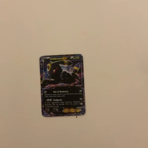 Pokémonkort Umbreon GX - Säljer ett Pokémonkort med Umbreon GX. Kortet har en mörk design med Umbreon i fokus och texten 'Veil of Darkness' och 'Endgame'. Perfekt för samlare eller Pokémon-entusiaster!