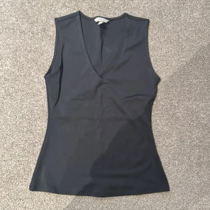Svart ärmlös topp från H&M - Snygg svart ärmlös topp från H&M med v-ringning. Perfekt för lager-på-lager eller som den är. Enkel och stilren design som passar till många olika outfits.