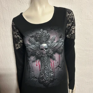Svart långärmad topp med dödskallemotiv - Cool svart topp med långärmade spetsdetaljer och ett stort dödskallemotiv på framsidan. Perfekt för en edgy look.