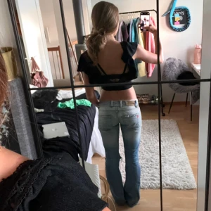 Svart offshoulder topp med öppen rygg  - Säljer en svart offshoulder topp med korta ärmar och croppad design. Toppen har en öppen rygg och volangdetaljer som ger en trendig look. Perfekt för sommarens varma dagar.