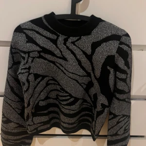 Svart och silvermönstrad tröja - Snygg svart tröja med ett iögonfallande silvermönster. Perfekt för att sticka ut med stil. Tröjan har långa ärmar. Perfekt för fina middagar och liknade. Köpte den för 349kr men säljer den för 125+frakt. Passar även för de som brukar ha M i storlek.