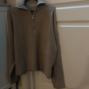 Beige ribbad tröja med dragkedja - Säljer en mysig beige tröja med ribbad struktur och dragkedja vid halsen. Perfekt för kyliga dagar med sin långa ärmar och bekväma passform.