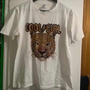 Vit t-shirt med leopardtryck - Snygg vit t-shirt med ett coolt leopardtryck och texten 'Cool Girl' i svart och brunt. Perfekt för en avslappnad stil med en touch av attityd.