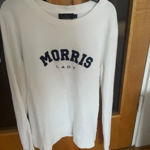 Vit långärmad tröja från Morris Lady - Säljer en stilren vit långärmad tröja från Morris Lady med mörkblå text på bröstet. Perfekt för en avslappnad och snygg look. Tröjan har en rund halsringning och är tillverkad i ett mjukt material. Knappt använd 