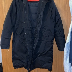 Svart parkajacka från Acne Studios - Snygg svart parkajacka från Acne Studios med lång ärm och huva. Jackan har en stilren design med knappar och dragkedja framtill. Perfekt för kyliga dagar. Vid fler frågor eller funderingar är det bara att höra av er. Pris kan diskuteras vid snabb affär😁