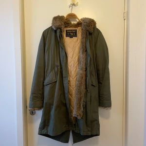 Grön parkajacka från Woolrich - Snygg och varm grön parkajacka från Woolrich med quiltat foder som går att ta bort vid varmare väder. 
