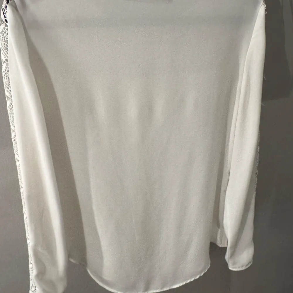 Elegant vit blus från Zara Basic med vackra spetsdetaljer på axlar och ärmar. Blusen har en rund hals och långa ärmar, perfekt för en stilren look.. Puserot.