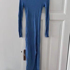 Blå ribbad klänning  - Snygg blå långklänning med ribbad struktur och snörning i bak. Klänningen har långa ärmar, perfekt för en stilren look.