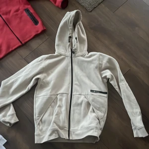 Beige huvtröja från Salo racing - Säljer en stilren beige huvtröja från Sail racing med dragkedja och praktiska fickor framtill.  Aldrig använd. Endast tvättad. Superfint skick. Strlk 176