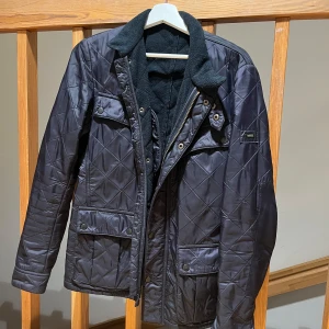 Svart quiltad jacka från Barbour - Snygg svart quiltad jacka från Barbour med dragkedja och knappar. Jackan har en mjuk krage och flera praktiska fickor. Perfekt för kyligare dagar. skick 9/10