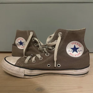 Ljus Bruna Converse All Star sneakers - Säljer ett par klassiska ljus bruna Converse All Star sneakers med vita snören och gummisula. Skorna har den ikoniska logotypen på sidan och är perfekta för en avslappnad stil.