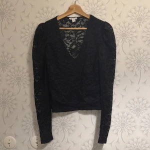 Svart spetsblus med v-ringning - Elegant svart spetsblus med v-ringad design och långa ärmar. Perfekt för en stilfull look med detaljerad spets som ger en sofistikerad touch.