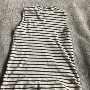 Randig ärmlös klänning🎀 - Säljer en stilren ärmlös klänning med svartvita ränder. Klänningen har en ribbad struktur och en liten brun knappdetalj med ett leende ansikte. Perfekt för en avslappnad och bekväm stil.💓💓