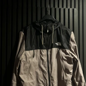Svart och beige vindjacka från The North Face - Säljer en stilren svart och beige vindjacka från The North Face. Jackan har en dragkedja framtill och en justerbar huva. Perfekt för blåsiga dagar och har en klassisk logga på bröstet.