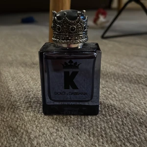 K by Dolce & Gabbana Eau de Toilette - Säljer en elegant herrparfym från Dolce & Gabbana. Flaskan är mörkblå med en kunglig krona som lock, vilket ger en lyxig känsla. Perfekt för den som vill ha en sofistikerad doft.