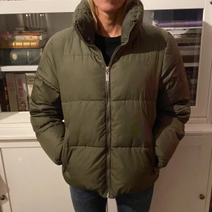 Olivgrön pufferjacka från Zink - Säljer en olivgrön pufferjacka från Zink med dragkedja framtill. Jackan har en hög krage och långa ärmar, perfekt för kyliga dagar. Den är stilren och enkel att matcha med olika outfits.