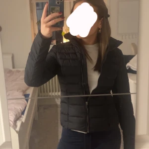 Svart pufferjacka från G2000 - Snygg svart pufferjacka från G2000 i storlek 34. Jackan har en dragkedja framtill och är perfekt för vårdagarna. Designen är en modern look och den är långärmad för extra värme. Dragkedjorna på fickorna går tyvärr inte att dra upp hela vägen men annars är den som ny, knappt använd. Säljer då den är för liten för mig och sitter alldeles för tajt. Skriv för fler bilder och skriv även innan ni trycker på köp direkt.