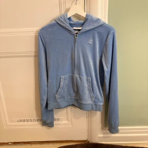 Blå velour hoodie och byxor från Juicy Couture - Säljer en mysig blå velour hoodie och matchande byxor från Juicy Couture. Hoodien har dragkedja och känguruficka, medan byxorna har resår i midjan. Perfekt för en avslappnad stil. 💙Det är också en liten fläck på vänstra sidan av dragkedjan och en liten fläck nere vid fötterna!