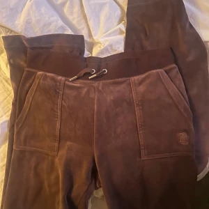 Bruna mjukisbyxor från Juicy Couture - Säljer ett par bruna mjukisbyxor från Juicy Couture med broderad logga. Byxorna har en bekväm passform med snörning i midjan och mjukt material.