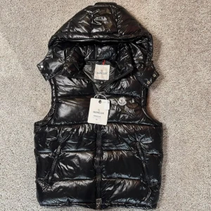  Moncler väst bytes - Snygg svart dunväst från Moncler med glansig finish och huva. Den är endast provad alla lappar är kvar - kan bytas mot förslag