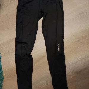 Svarta leggings från Newbody - Snygga svarta leggings från Newbody, perfekta för träning. De har en tight passform och är tillverkade i ett stretchigt material för bästa komfort. Diskret logga på benet. Som vistat på bild 2 finns det ett litet hål på knät.