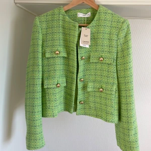 Grön kavaj från Mango L oanvänd - Snygg grön kavaj från Mango i ett strukturerat tyg med guldknappar. Kavajen har en klassisk design med fyra fickor framtill och rund halsringning. Perfekt för att ge en färgklick till din outfit.