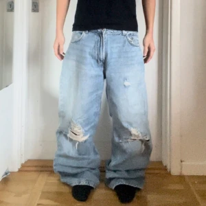 Ljusa baggy jeans - Säljer ett par ljusa baggy jeans med slitningar på knäna. De har en avslappnad passform -baggy. Jeansen har klassisk femficksdesign och knappgylf.