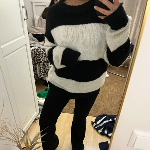 Randig stickad tröja - Mysig stickad tröja med breda svarta och vita ränder. Tröjan har en avslappnad passform och långa ärmar, perfekt för kyligare dagar.