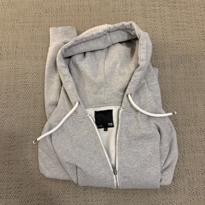 Grå hoodie från Lager 157 - Säljer en klassisk grå hoodie från Lager 157 i storlek XL, passar mer L dock. Den har en dragkedja framtill och justerbar huva med snören. Perfekt för en avslappnad stil. Använd vid väldigt få tillfällen