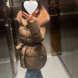 Brun dunjacka med pälsdetalj - Hej Tjejer!! Jag säljer en snygg brun dunjacka med stor pälskrage och bälte i midjan. Perfekt för kalla dagar med sin varma och puffiga design. Jag köpte den för 2 månader sen från Fur stockholm. Pris kan diskuteras☺️