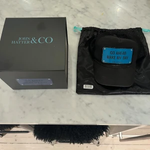 Svart keps från John Hatter & Co - Säljer en snygg svart keps från John Hatter & Co med texten 'GO AHEAD MAKE MY DAY' framtill. Kepsen har ett nätmaterial på baksidan för bättre ventilation och justerbar passform. Man får med alla tillbehör. Nypris är 995kr. Skicket är ganska bra och har använt kepsen några gånger.