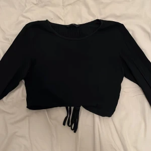 Svart croppad topp med knytband - Snygg svart croppad topp med långa ärmar och knytband på ryggen. 