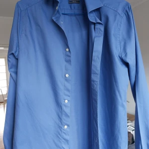 Blå skjorta från Riley - Snygg blå skjorta från Riley i slim fit. Skjortan har långa ärmar och knappar framtill. Perfekt för en stilren look.