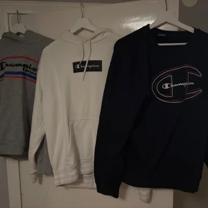Champion hoodies i olika färger - Tre snygga hoodies från Champion i grått, vitt och mörkblått. De har långa ärmar och klassisk Champion-logga på bröstet. Perfekta för en avslappnad stil. Bra kvalitet! Paketpris går att lösa