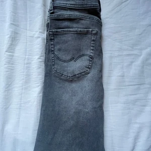 Grå slim fit jeans från Jack & Jones - Snygga grå jeans från Jack & Jones med klassisk femficksdesign. De har en normal passform och är perfekta för en avslappnad stil. Jeansen har en knappgylf och är tillverkade i ett slitstarkt material. Storleken är 170/164 men mätningarna är ungefär 28/30
