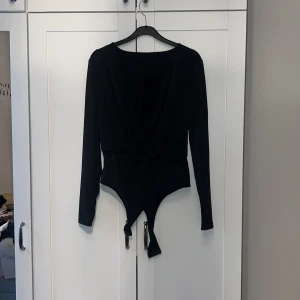 Svart omlott body - Snygg svart omlott body med långa ärmar och djup v-ringning. Perfekt för en stilren look. Tillverkad i ett mjukt och stretchigt material för en bekväm passform.