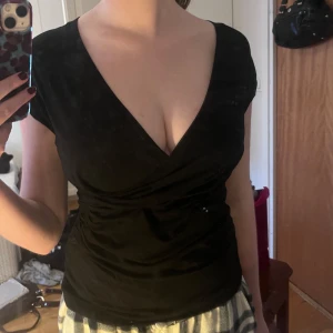 Svart omlottopp - Snygg svart omlottopp med v-ringning och korta ärmar. Perfekt för en stilren look. Tillverkad i ett mjukt och bekvämt material. Går att justera så man kan ha den på båda/inga/en axel 🤩😍 Den är ej croppad! Skriv om du har frågor 💗💪🏻