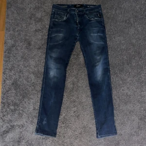 Blå jeans från Replay - Snygga blå jeans från Replay i modellen Anbass hyperflex. De har en klassisk femficksdesign med en lätt tvättad look och Replay-logga på bakfickan. Perfekta för en avslappnad stil. Pris går att diskutera. Storlek 31/32 men sitter mer som 30 i midjan. Alla slitningar är design. Liten fläck på benet men går bort i tvätten