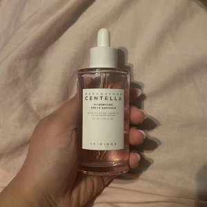 Centella Redermizing Ampoule från Skin1004 - Säljer en Centella Redermizing Fresh Ampoule från Skin1004. Den kommer i en genomskinlig glasflaska med pipett och innehåller en ljusrosa vätska. Perfekt för att återfukta och lugna huden.