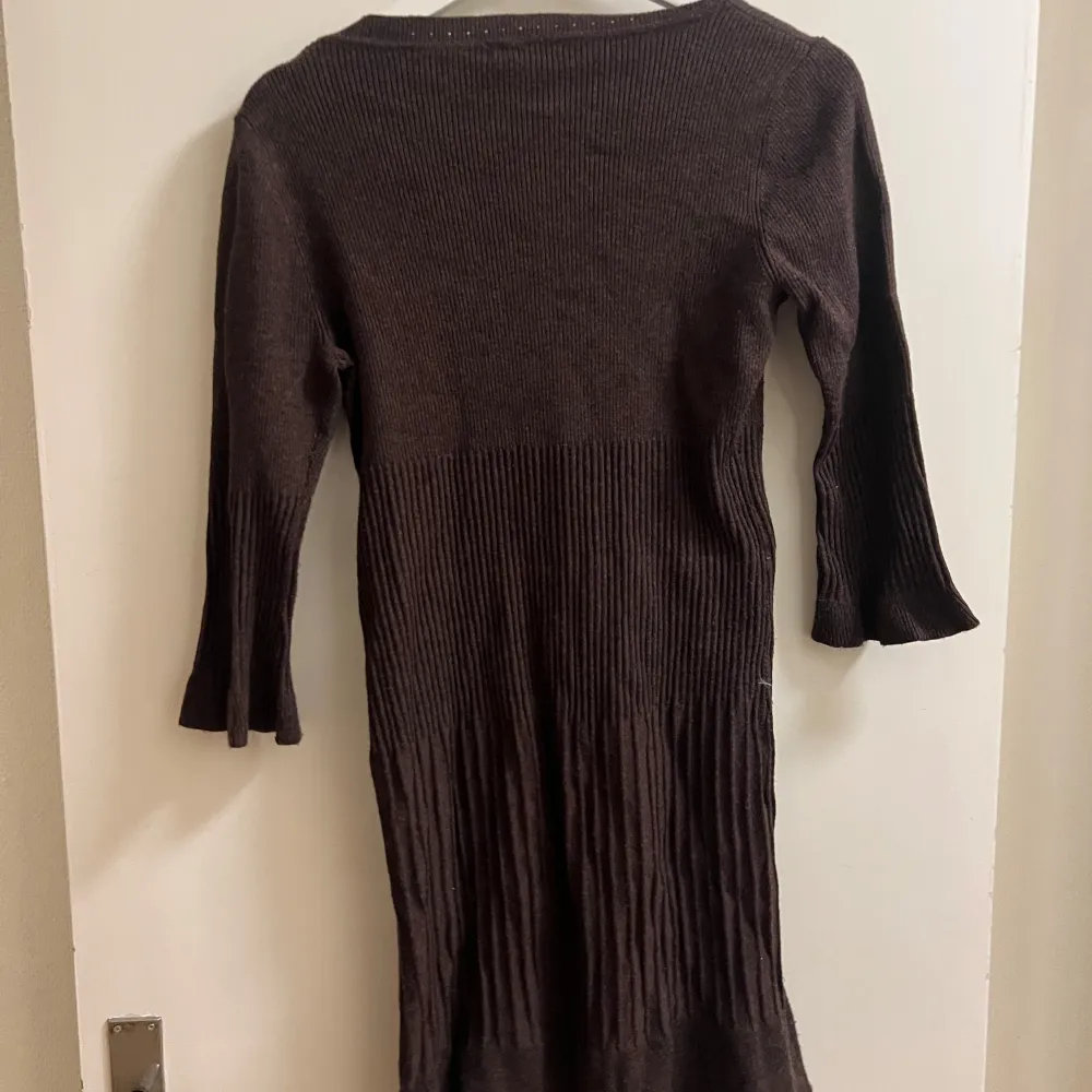 Säljer en brun stickad klänning från H&M med trekvartsärmar och ribbad struktur. Perfekt för höst och vinter med sin mysiga design. Klänningen har en rund halsringning och en figurnära passform.. Mekot.