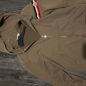 Brun hoodie med dragkedja från Moncler - Säljer en snygg brun hoodie från Moncler med dragkedja och huva. Köpt på Kasperheat. Jag är öppen för byten endast! Storlek M men sitter bättre på S och Xs köpt är köpt!