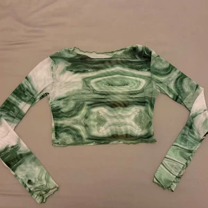 Grön och vit mesh mönstrad croppad topp - Snygg croppad topp med ett unikt grönt och vitt mönster i mesh. Toppen har långa ärmar och en tight passform, perfekt för att sticka ut i mängden.