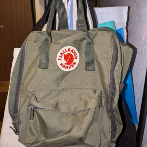 Militärgrön ryggsäck från Fjällräven - Säljer en klassisk grön Fjällräven Kånken ryggsäck. Den har ett stort huvudfack, en mindre frontficka och två sidofickor. Ryggsäcken har justerbara axelremmar och ett handtag upptill. Perfekt för både vardag och äventyr!