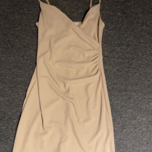 Beige omlottklänning - Snygg beige omlottklänning med smala axelband och v-ringning. Perfekt för en stilren look. Den är från HM och aldrig använd❤️Kort klänning som är över knäna på mig❤️